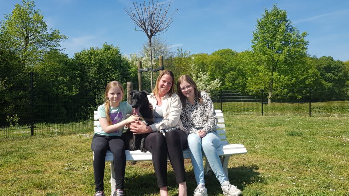 We zien drie vrouwen op een bankje in een omheind veld. Het zijn de initiatiefnemers van het hondenspeelveld in Herkenbosch. Hun hond is ook zichtbaar op de foto.