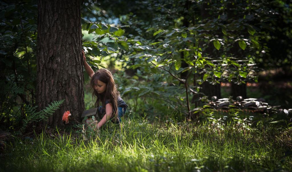 Een meisje bukt naast een boom in het bos.
