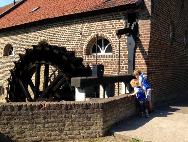 Het bovenste deel van het wiel van de Gitstappermolen. Rechts zien we twee kinderen die over een muurtje naar beneden kijken om te kijken hoe het wiel water rondpompt.